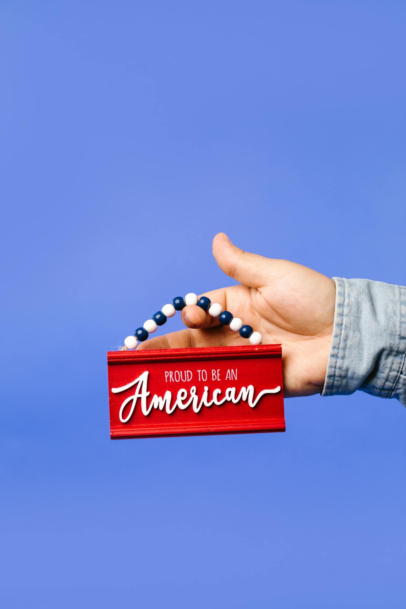 Hand holding a red American pride sign against a blue backdrop, symbolizing patriotism.
