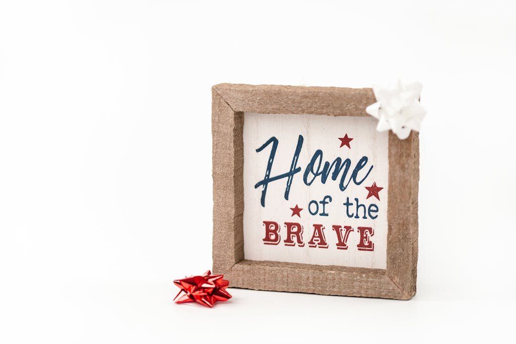Patriotic framed sign with 'Home of the Brave' text and festive bows, perfect for home decor.